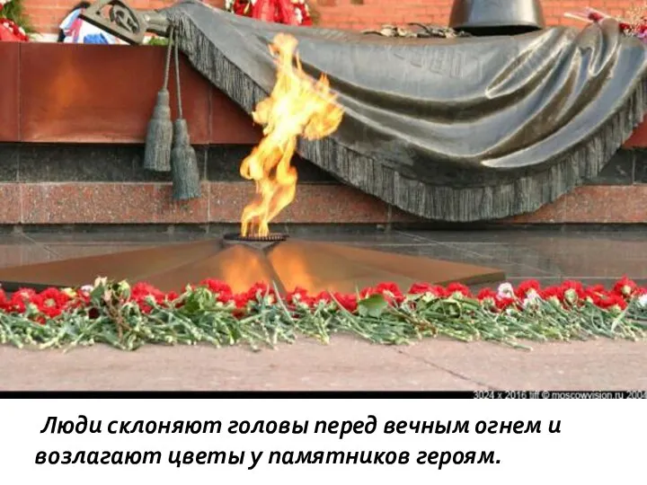Люди склоняют головы перед вечным огнем и возлагают цветы у памятников героям.